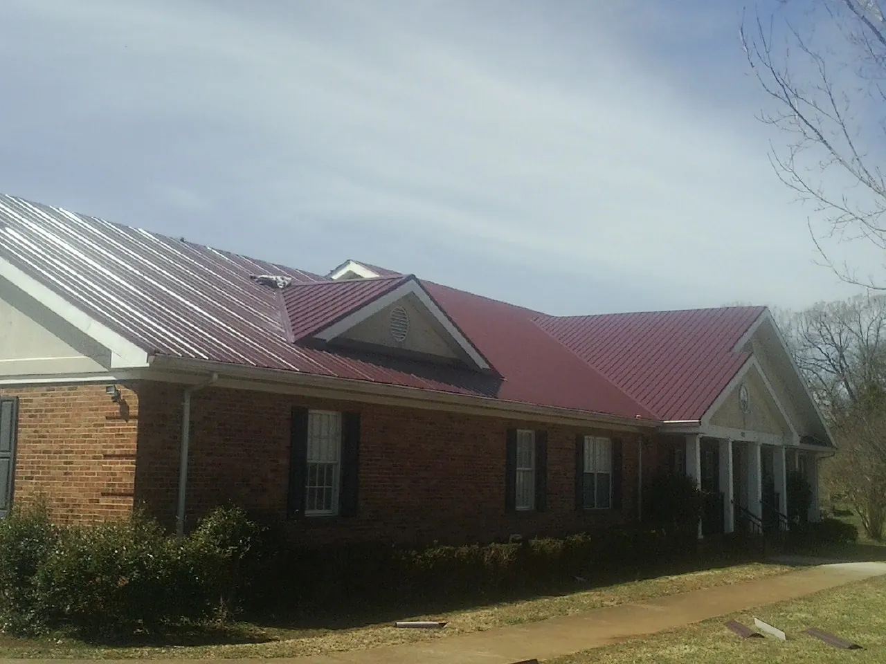 Red metal roof with gabled entries on a long brick building, from a Hail Damage Roof Repair job in Amana