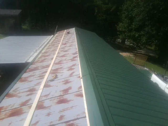 Old rusted panels beside newly installed green metal roofing — Wind Damage Roof Repair by Roofing Brothers in Amana