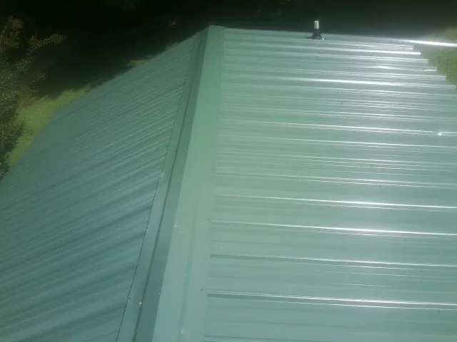 New green metal panels meeting at the ridge of a roof — Flat Roof Repair work by our crew in Amana