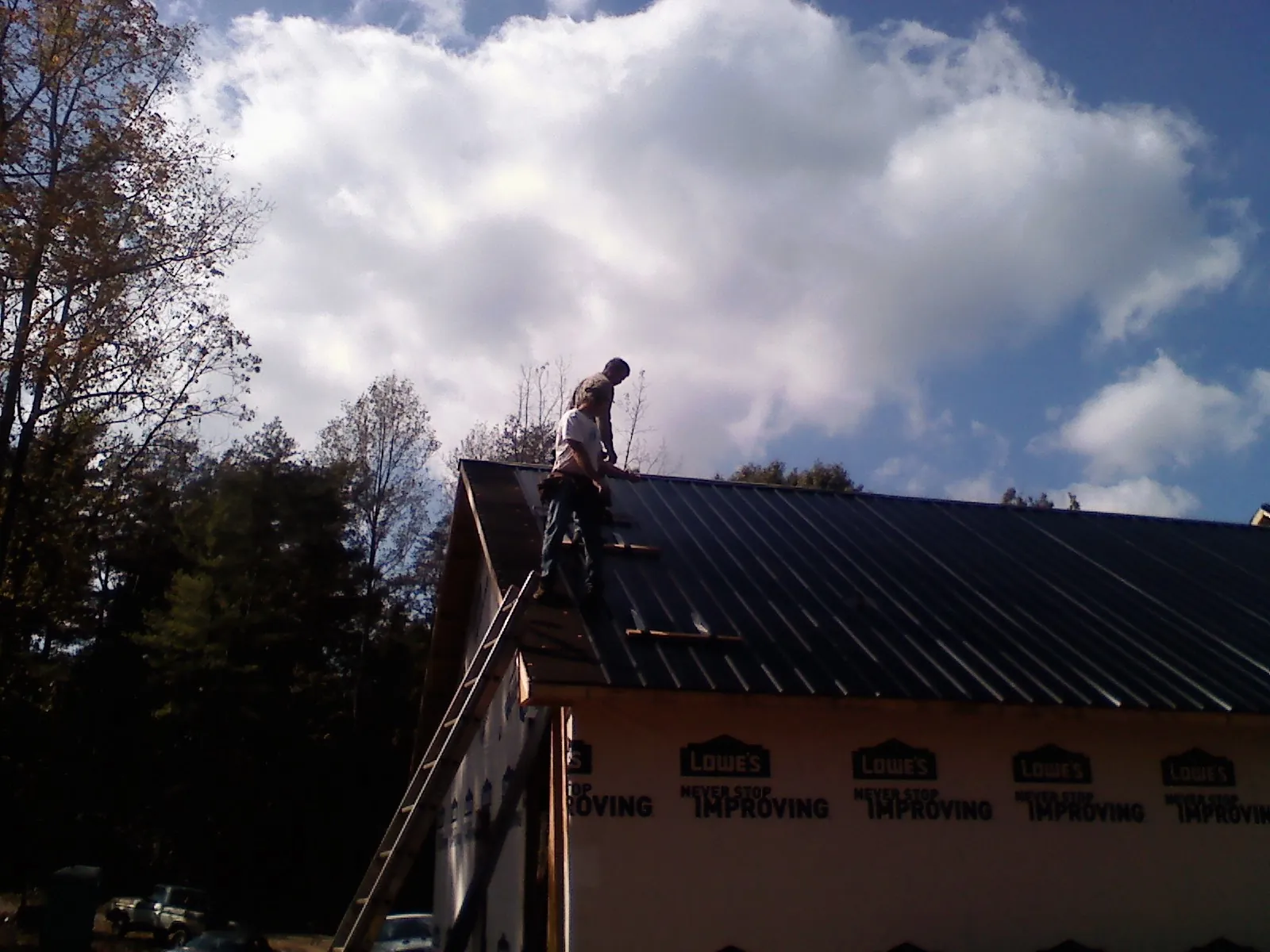 Roofer fastening dark metal panels high against a cloudy sky, from a Roof Inspection job in Amana