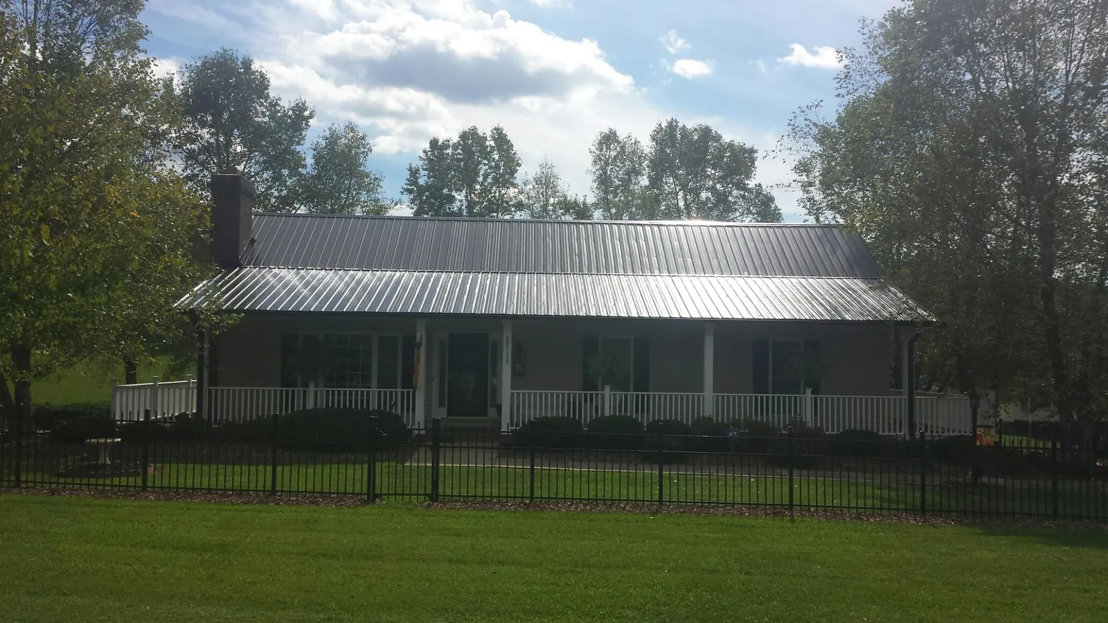Gray metal roof on a brick ranch with a full width front porch — Gutter Guard Installation work by our crew in Amana