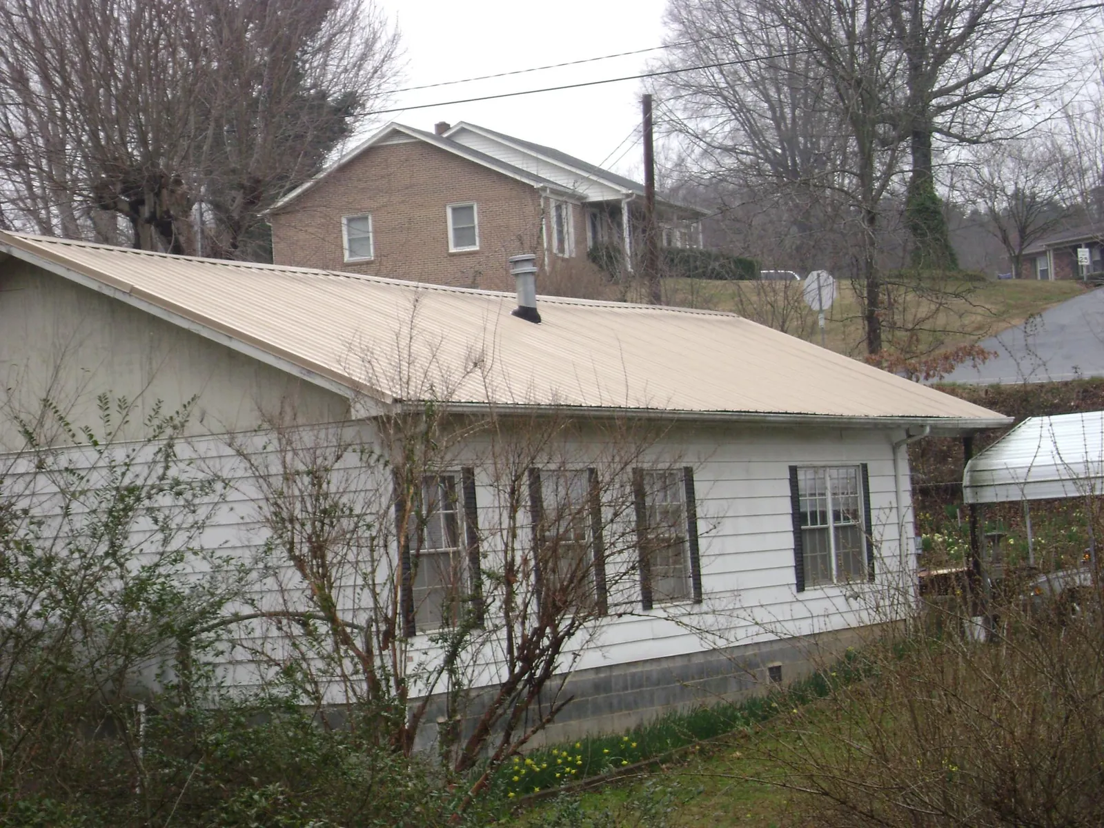 Tan metal roof on a white sided house set into a hillside — Commercial Roofing by Roofing Brothers in Amana