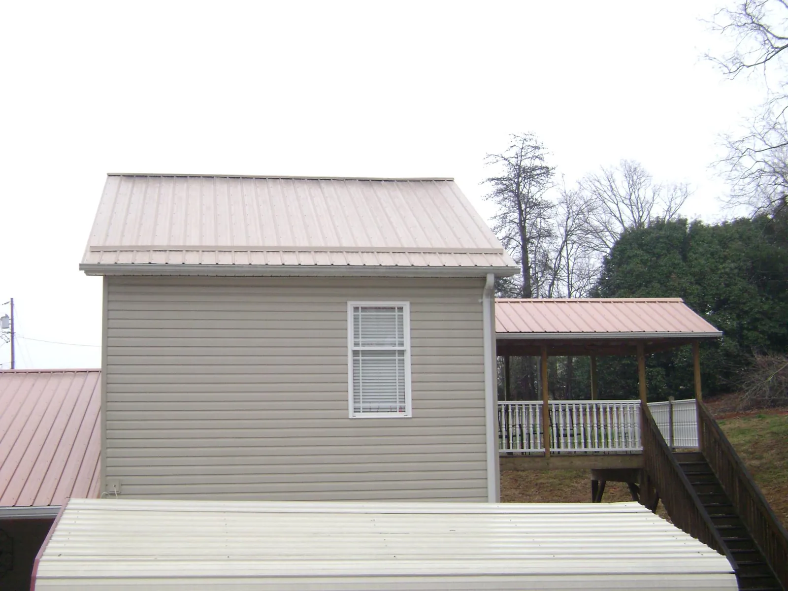 Tan metal roofs on a two story addition and attached porch, from a Roof Replacement job in Amana