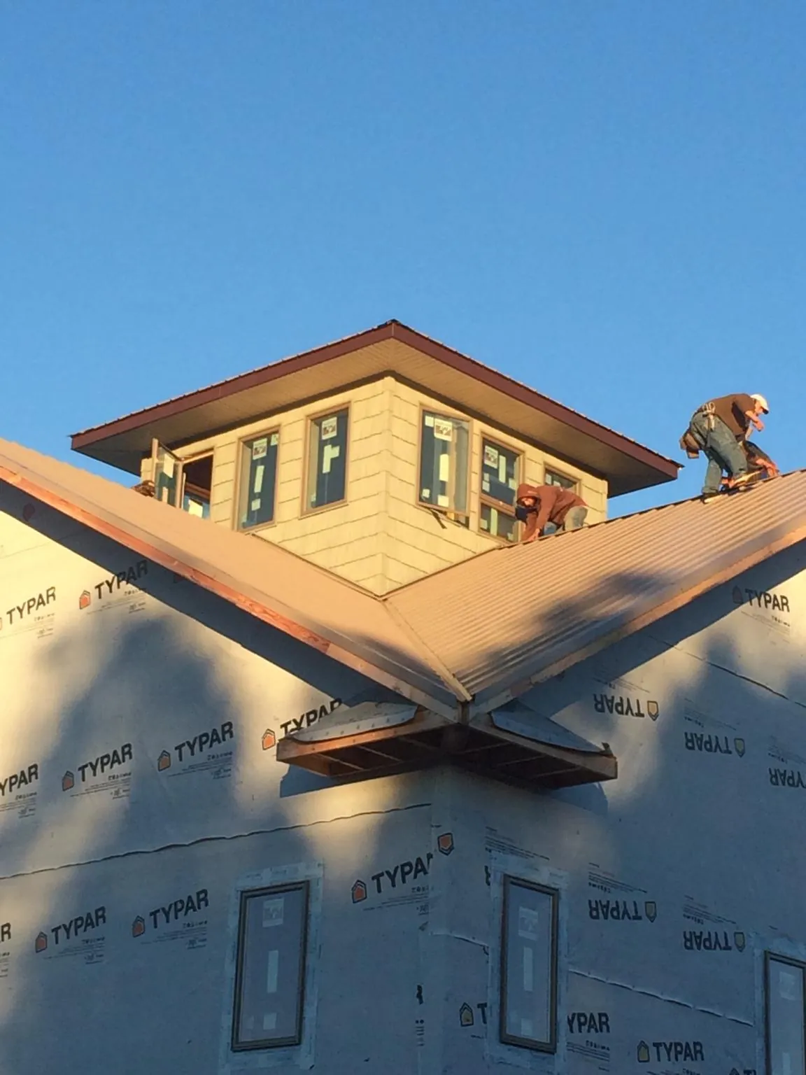 Roofers working around a rooftop cupola on a new metal roof at sunset — Roof Waterproofing in Amana by Roofing Brothers